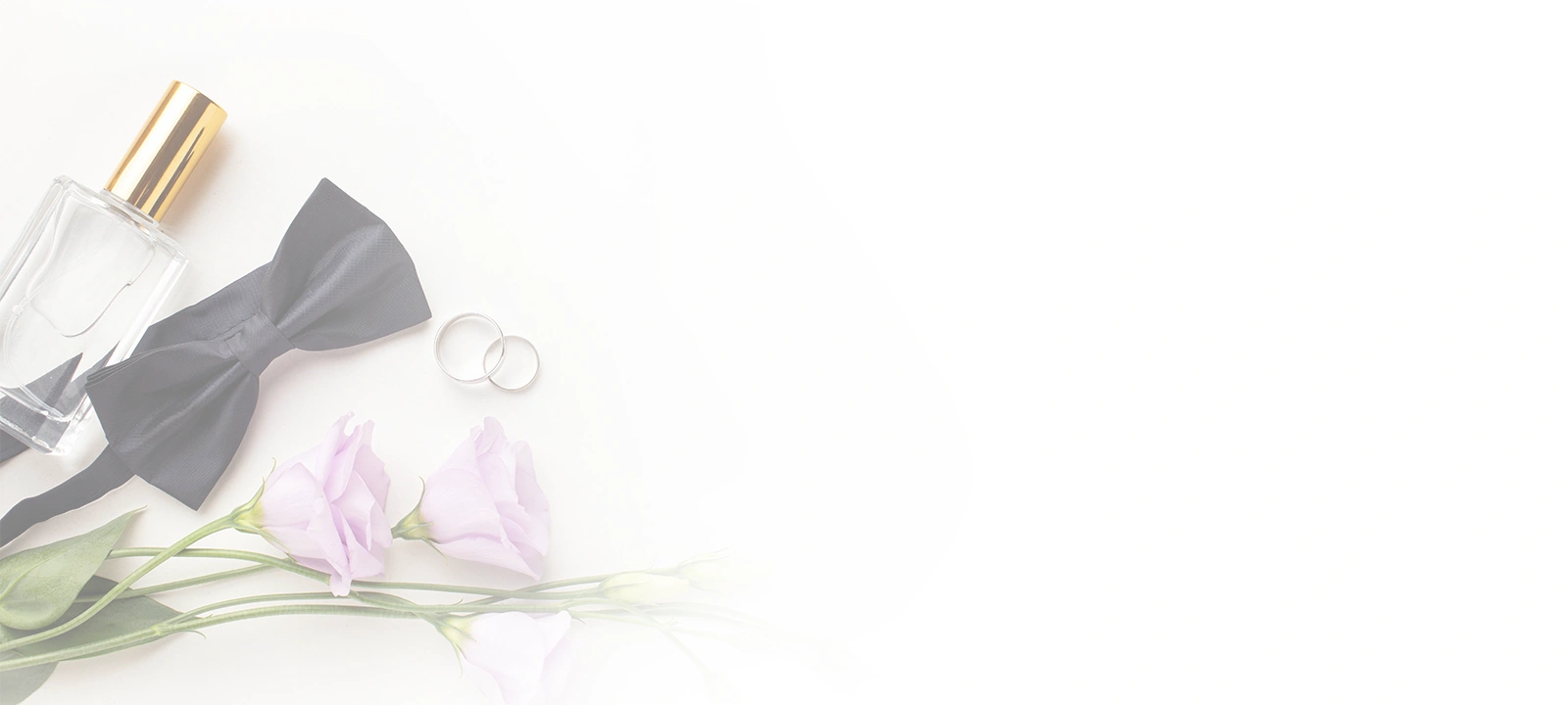 Flat lay of wedding items including a black bow
                                    tie, two silver wedding rings, a perfume bottle, and
                                    light purple flowers on a white background.